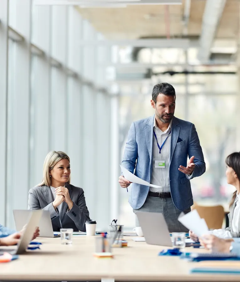 Business leader presenting to a diverse team in a modern office conference room, discussing workforce management strategies and collaboration.