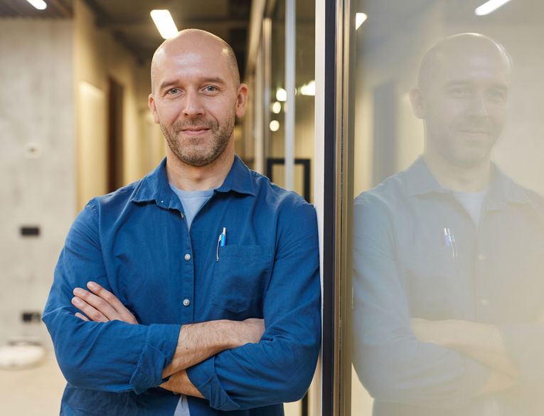 Mand i afslappet kontormiljø, der udstråler tillid og professionalisme, perfekt til promovering af karrieremuligheder inden for arbejdsstyring, vagtplanlægning og tidsregistrering