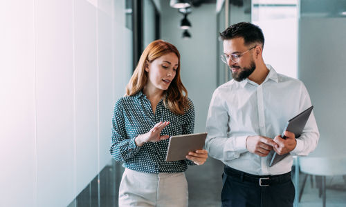 Two colleagues walking through the office collaborating on a tablet, illustrating data-driven workforce management, modern HR processes, and efficient staffing planning.