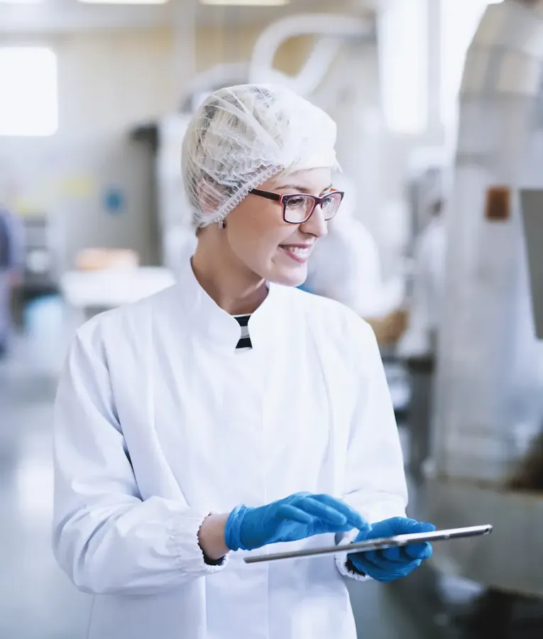 Smiling female worker in a food processing plant using a tablet for quality control and workflow management. Represents digital workforce solutions in food production.