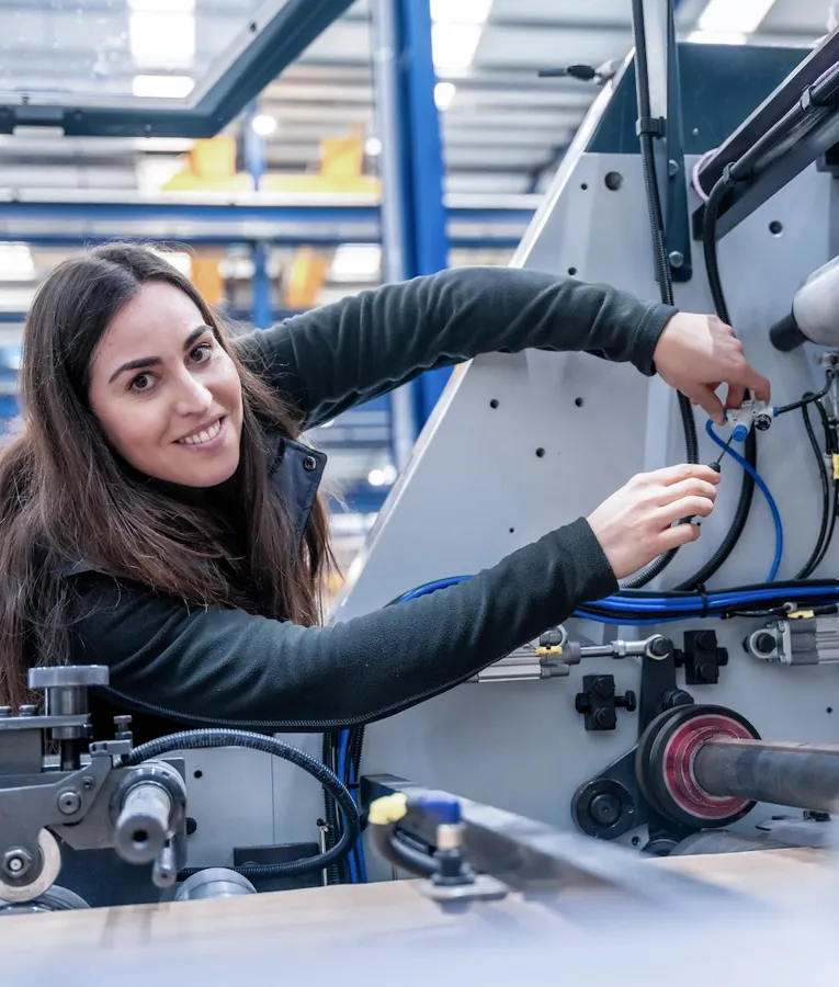 Female technician working on factory machinery, scheduled on a shift using workforce management tools with task-based time tracking for manufacturing efficiency.