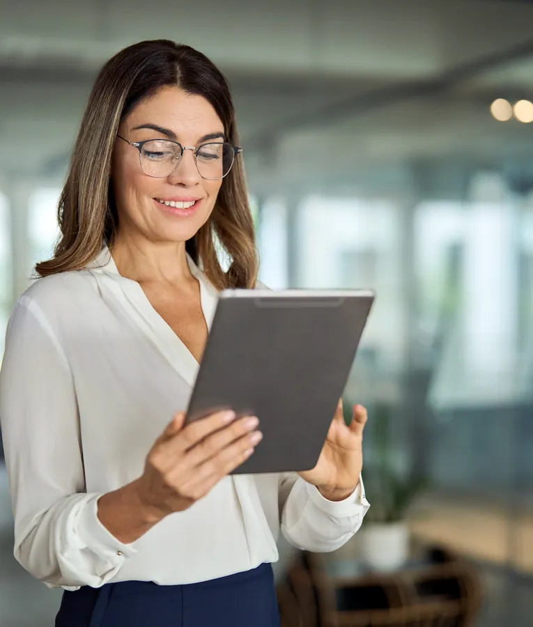 A cheerful businesswoman in a white blouse sits at her desk, talking on the phone while using her laptop. The image conveys productivity, communication, and efficient workplace management.