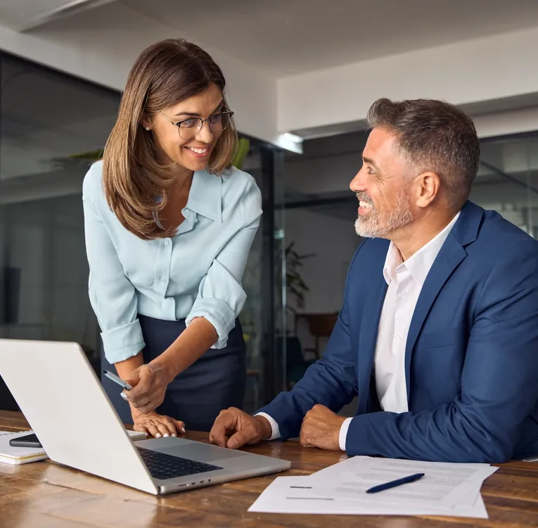 Smiling business professionals collaborating in a modern office, discussing data on a laptop. Represents teamwork, leadership, and efficient workforce management.