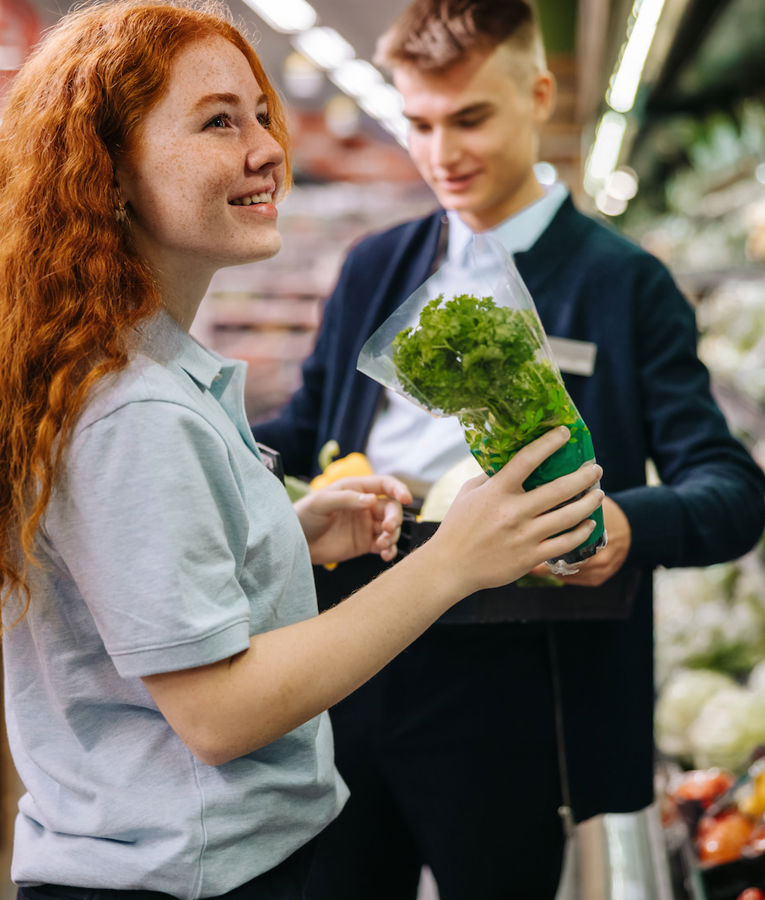 A friendly retail employee helping a customer select fresh organic produce, enhancing customer satisfaction in grocery retail.