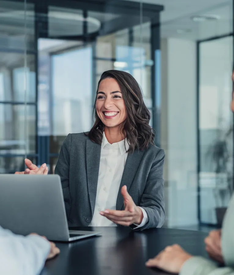 Smilende forretningskvinde præsenterer workforce management-strategier for kollegaer i mødelokale med fokus på vagtplanlægning og digital tidsregistrering.