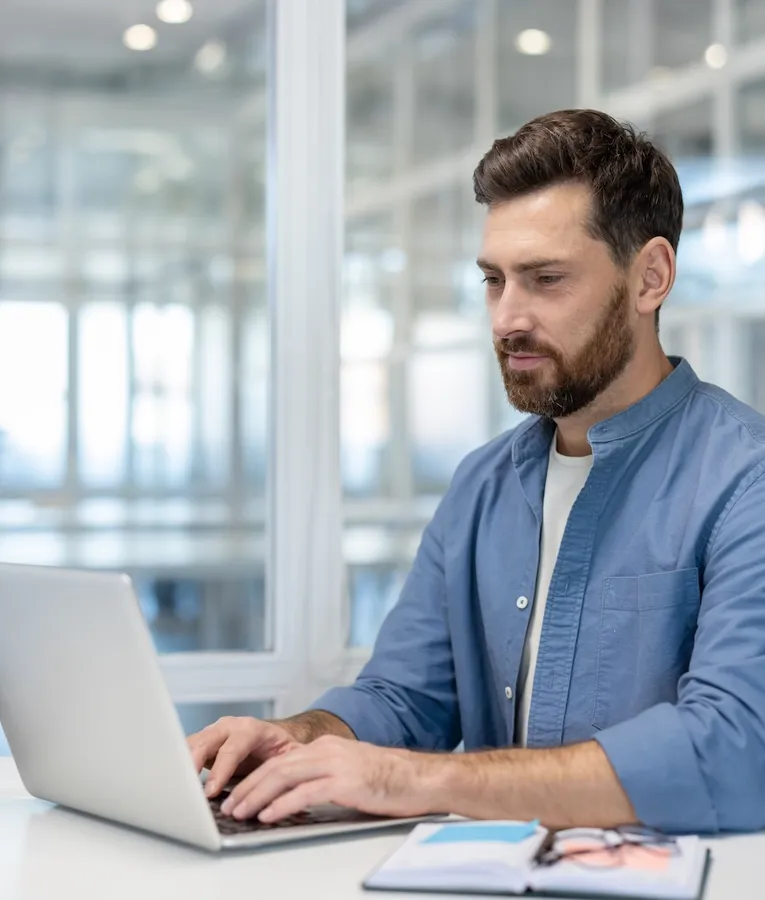 Office employee working on a laptop in a modern workspace, using digital workforce management tools for scheduling, time tracking, and HR planning.