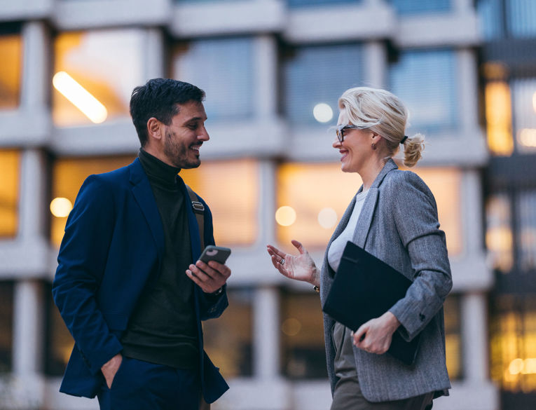To kolleger i forretningsmiljø, der diskuterer arbejdsstyring, vagtplanlægning og tidsregistrering ved hjælp af en mobil enhed