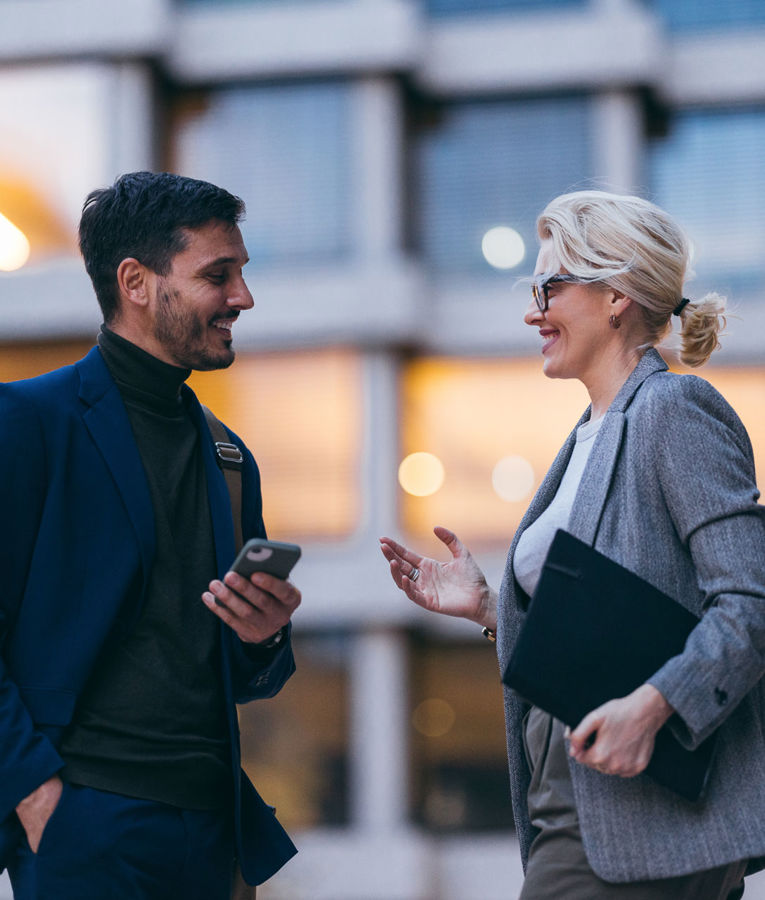 Two colleagues in a business setting discussing workforce management, scheduling, and time tracking using a mobile device