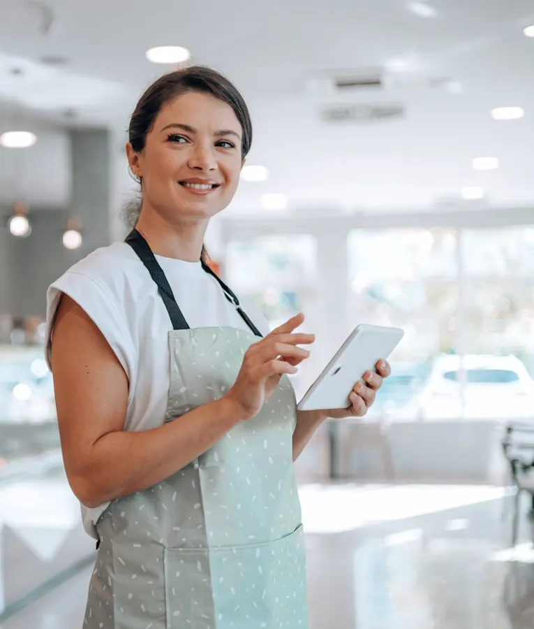 Smiling bakery employee using a tablet for inventory or order management in a modern café, showcasing digital workforce solutions.