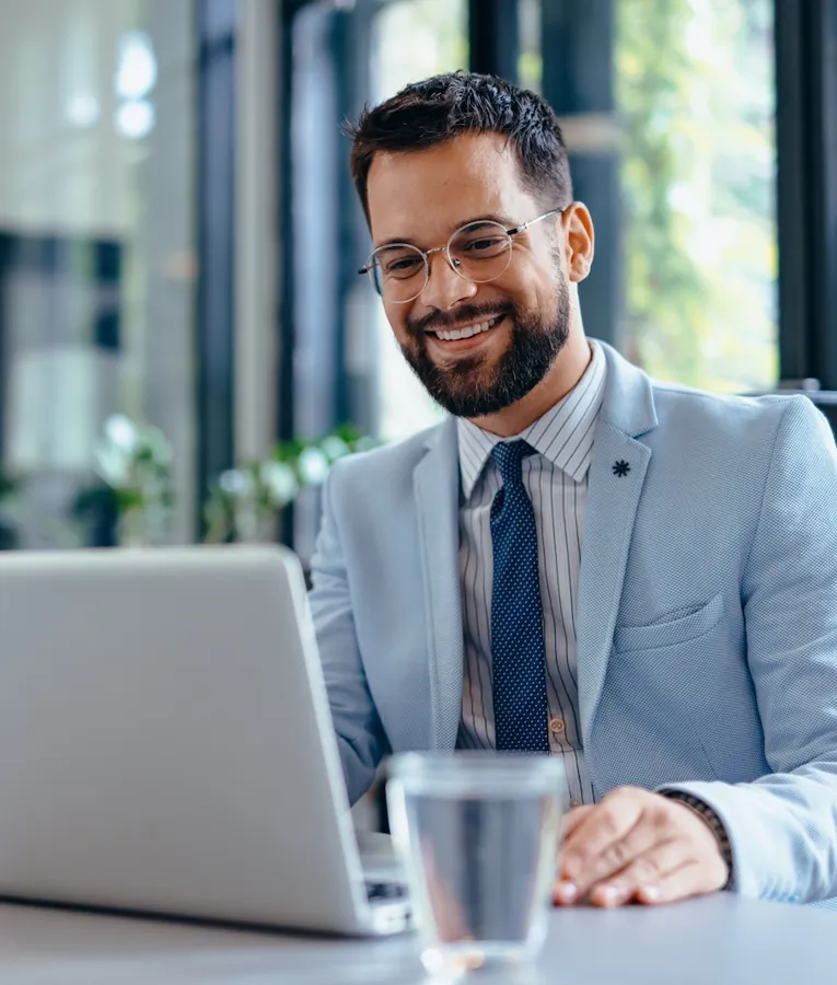 Smiling businessman in a modern office working on a laptop, managing workforce operations and business strategies. Represents digital productivity and leadership.
