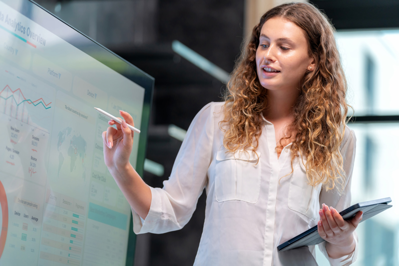 Woman presenting data and AI analytics on a large screen as part of a presentation on workforce management, efficient staff scheduling, and time tracking within the company.